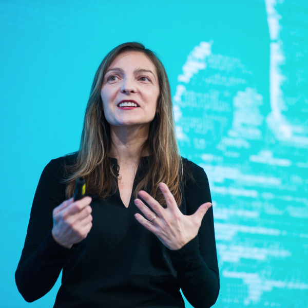 Woman smiling and speaking emphatically with her hands against a bright blue-green background