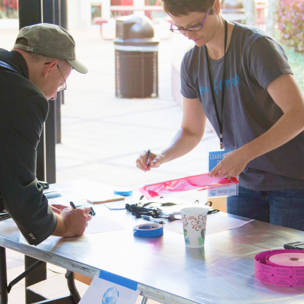 Woman volunteer helps man sign-up at World IA Day event table